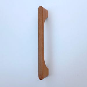 May include: A wooden cabinet door pull with a curved design. The pull is a light brown color.