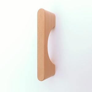 May include: A light brown wooden cabinet door pull with a curved cutout. The pull is made of solid wood and has a smooth finish.