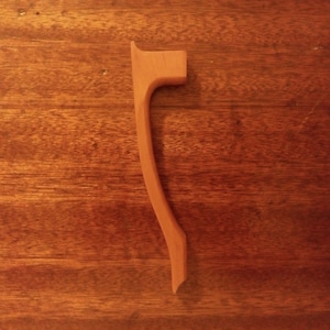 May include: A single, light brown wooden object with a curved design. The object has a flat top and a pointed bottom. The wood grain is visible. The object is likely a decorative or functional item.