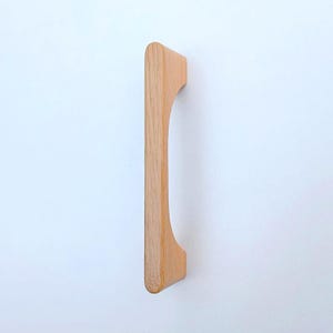 May include: A light wood cabinet pull with a curved design. The pull is made of solid wood and has a natural finish.