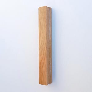 May include: A wooden door handle with a simple, rectangular design. The handle is made of light brown wood and has a smooth finish.