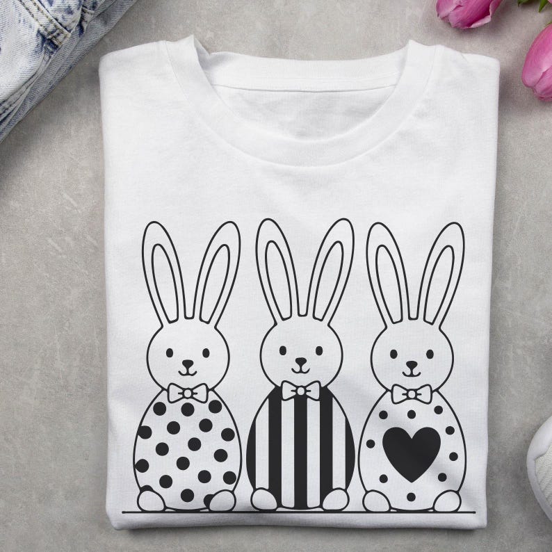 K&ouml;nnte beinhalten: Wei&szlig;es T-Shirt mit einem schwarz-wei&szlig;en Design von drei Cartoon-Hasen mit Fliegen. Die Hasen haben Punkte-, Streifen- und Herzmuster.