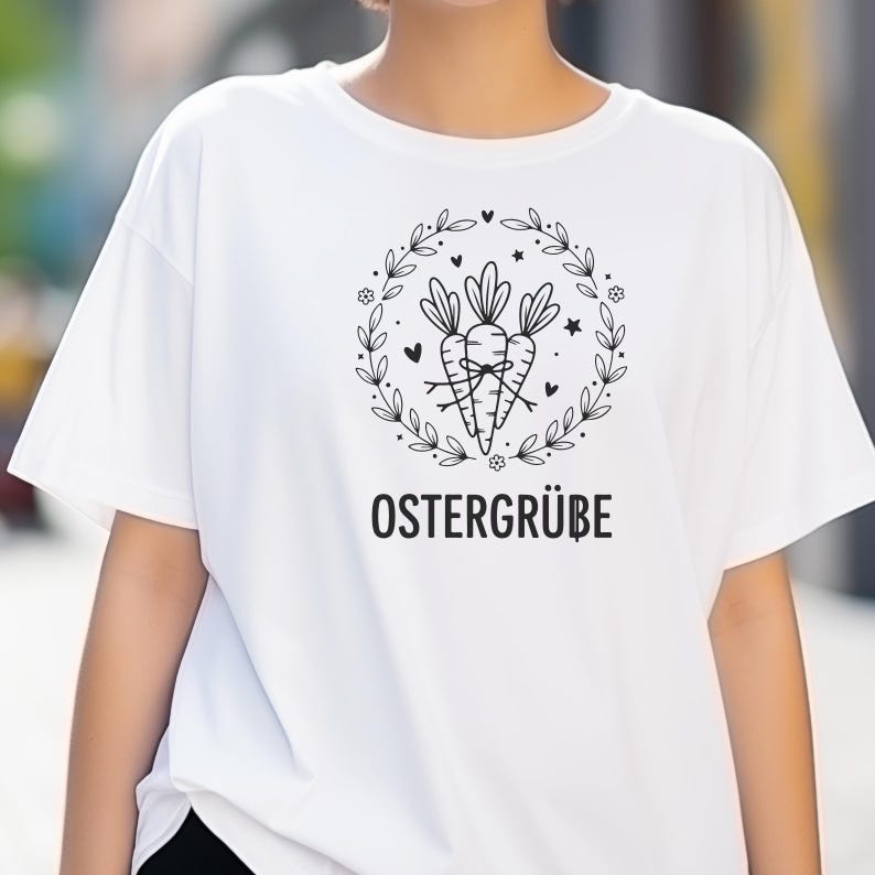 K&ouml;nnte beinhalten: Wei&szlig;es T-Shirt mit einer schwarzen Grafik von drei Karotten, die zusammengebunden sind und von einem floralen Kranz mit Herzen und Sternen umgeben sind. Der Text "OSTERGR&Uuml;BE" ist darunter gedruckt.