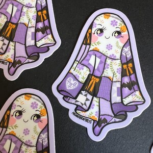 Op de afbeelding: Verschillende stickers met een cartoongeest met een patchwork quilt ontwerp in tinten paars, wit en bruin. De geest heeft een lachend gezicht met roze wangen en oranje accenten. De stickers hebben een lichtpaarse rand en de tekst "foxandrambles".