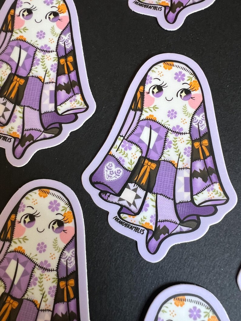 Op de afbeelding: Verschillende stickers met een cartoongeest met een patchwork quilt ontwerp in tinten paars, wit en bruin. De geest heeft een lachend gezicht met roze wangen en oranje accenten. De stickers hebben een lichtpaarse rand en de tekst "foxandrambles".