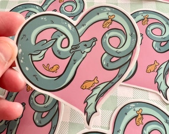 May include: A sticker featuring a blue sea serpent in a heart shape with a pink background. The serpent is curled around itself and has a small, cute face. There are small yellow fish swimming around the serpent.