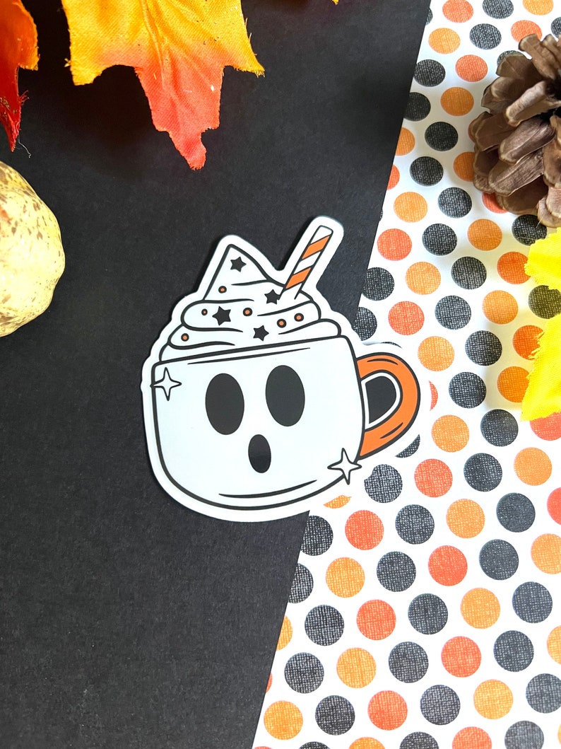 May include: A white ghost-shaped coffee cup with a black and white whipped cream topping and a red and white straw. The cup has a black outline and a black handle. The background is a black and white polka dot pattern.
