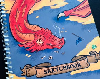 Może przedstawiać: Szkicownik w oprawie spiralnej z ilustracją czerwonego smoka. Smok pali, otoczony elementami fantasy, takimi jak klejnoty, miecz i baner z napisem "SKETCHBOOK". Okładka ma niebiesko-żółte tło.