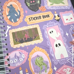 May include: A spiral-bound sticker book with a purple cover. It features framed illustrations of a werewolf, a frog, ghosts, and other whimsical creatures. The words "STICKER BOOK" are printed on a yellow banner.