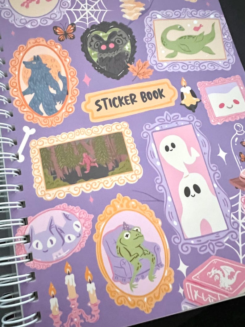 May include: A spiral-bound sticker book with a purple cover. It features framed illustrations of a werewolf, a frog, ghosts, and other whimsical creatures. The words "STICKER BOOK" are printed on a yellow banner.