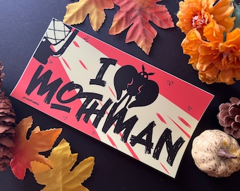 May include: A pink and cream sticker with black text that reads "I love mothman". A black silhouette of a mothman is in the center of the sticker.