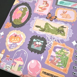 May include: A spiral-bound notebook with a purple cover featuring framed illustrations of whimsical creatures and objects. A butterfly, a crystal ball, and the text "FOXANDBRAMBLES" are also visible. The illustrations are in various colours.