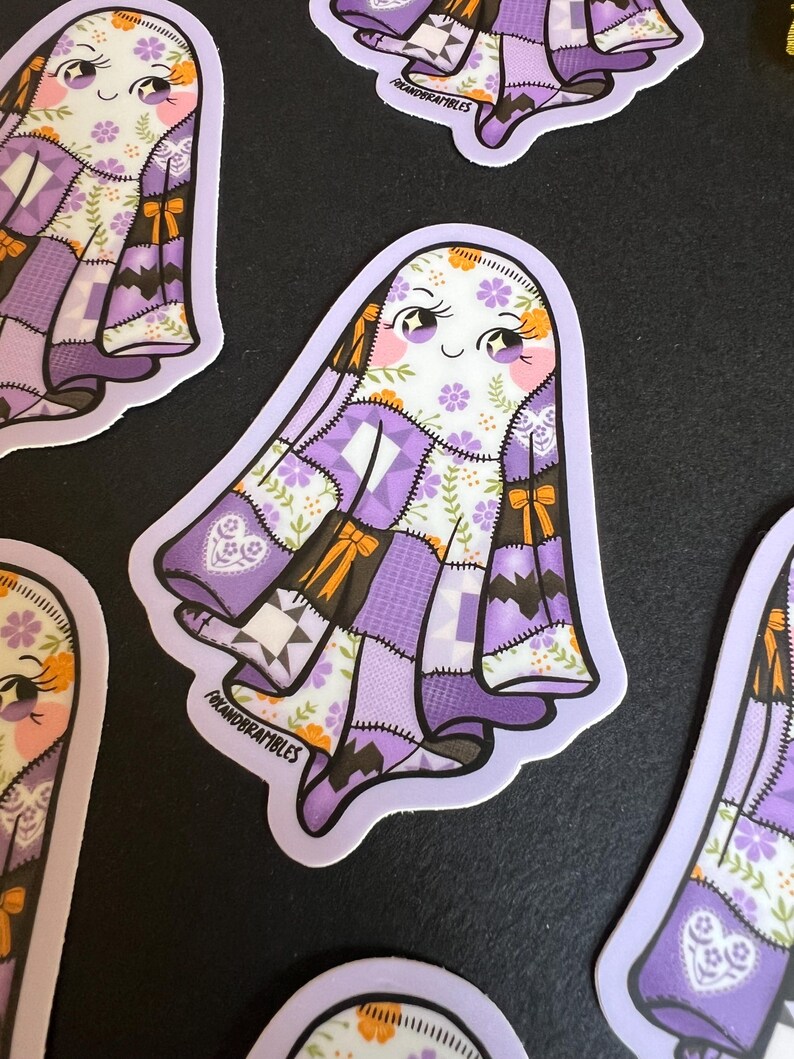 Op de afbeelding: Een verzameling stickers met een vriendelijk spookontwerp. Het spook heeft een patchwork-stijl lichaam in tinten paars, wit en bruin, met bloemen- en strikaccenten. De stickers hebben een lichtpaarse rand en een lachend gezicht.