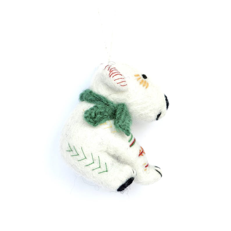 May include: A white felt polar bear ornament with a green scarf. The bear has black paws and eyes, with red and green embroidered details. The ornament is approximately 4 inches tall.
