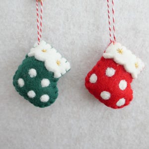May include: Two felt Christmas stocking ornaments. One is green with white polka dots, the other is red with white polka dots. Both have white scalloped tops with gold star accents and are suspended by red and white twine.