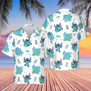 Könnte beinhalten: Weißes Hemd mit Hawaii-Print mit einer blauen Cartoon-Figur, Ananas, blauen Hibiskusblüten und Regenschirmen. Das Hemd hat kurze Ärmel und einen klassischen Kragen. Der Hintergrund zeigt eine Strandszene.