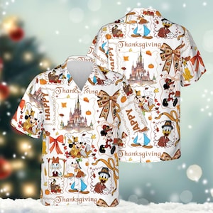 Może przedstawiać: Biała koszula z krótkim rękawem z motywem Święta Dziękczynienia. Wzór zawiera postacie z kreskówek, zamki, dynie i napisy "Happy Thanksgiving". Koszula ma dekolt w serek.