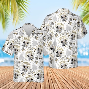 Op de afbeelding: Wit overhemd met korte mouwen met een herhalend patroon van Mickey Mouse, klokken, champagneglazen en het jaar "2026" in goud en grijs. Het overhemd heeft een kraag. De achtergrond toont een strandscène.