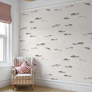 May include: A room with white walls adorned with a repeating pattern of gray fish illustrations. A striped armchair with a red and white striped pillow sits in the corner. The room has a beige carpet and a window with a pink shade.
