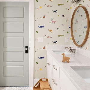 May include: A bathroom featuring wallpaper with a colorful animal pattern, a light gray door with a black handle, a white vanity with a marble countertop, a wooden oval mirror, a wooden duck toy, and a wooden step stool on a black and white polka dot floor.