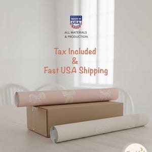 May include: Two rolls of wallpaper, one pale pink with a bow design and one white, are displayed on a table. A cardboard box is beneath the pink roll. The image includes the text "Made in USA".