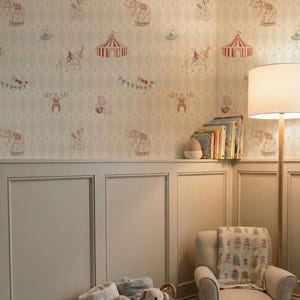 May include: A room decorated with circus-themed wallpaper showing elephants, acrobats, and tents. There's a light-coloured armchair with a blanket, a basket of soft toys, and a floor lamp. The walls are painted in a neutral colour.