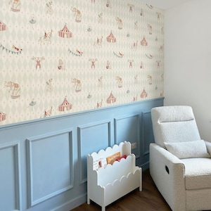 May include: A nursery room with circus-themed wallpaper featuring elephants, tents, and performers. The room has light blue panelling, a white scalloped bookshelf, a white recliner chair, and a dark wood floor.
