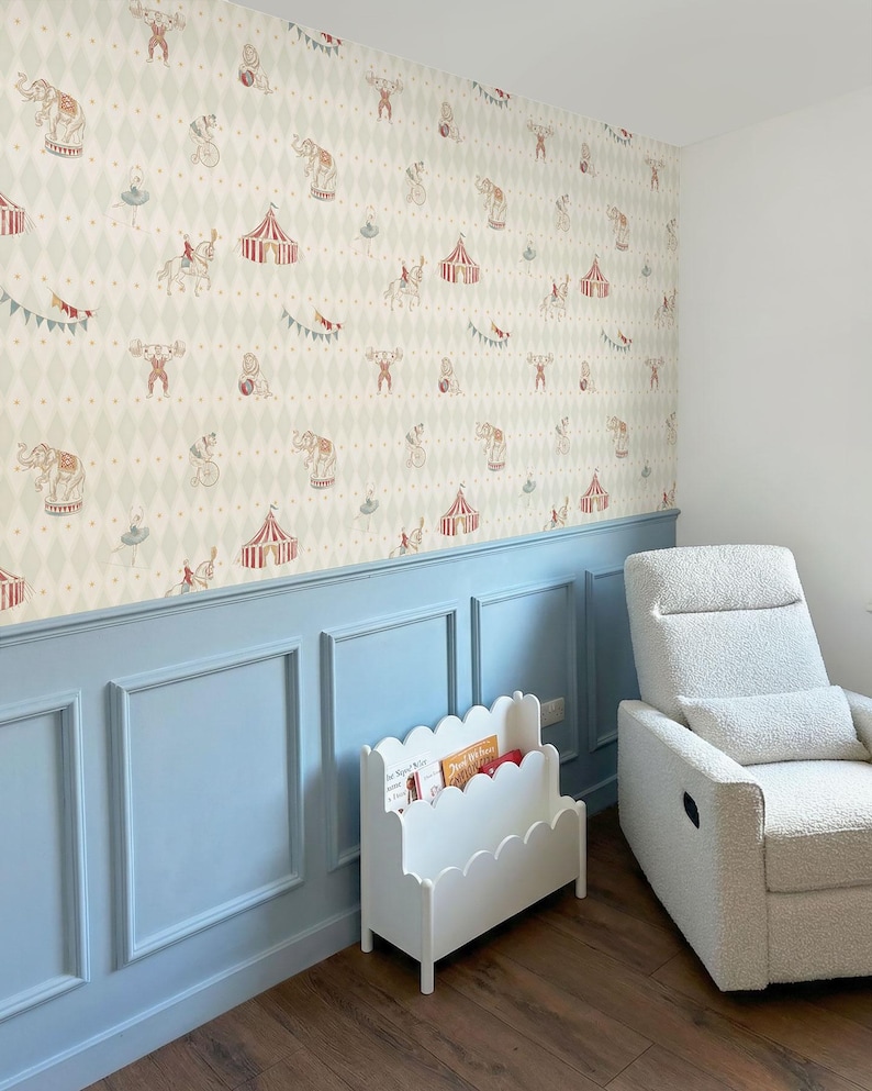 May include: A nursery room with circus-themed wallpaper featuring elephants, tents, and performers. The room has light blue panelling, a white scalloped bookshelf, a white recliner chair, and a dark wood floor.