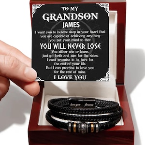 May include: A black braided leather bracelet with a magnetic clasp engraved with the words love you forever, presented in a dark wood box with a card that reads To My Grandson James, I want you to believe deep in your heart that you are capable.