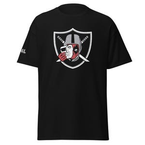 May include: A black short-sleeve t-shirt featuring a graphic on the chest of a shield with two crossed swords. Inside the shield is a character wearing a helmet and holding a white mask over their face. The text 4L is printed on the right sleeve.