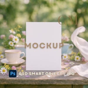 Puede incluir: Una tarjeta de maqueta rectangular blanca con la palabra "MOCKUP" en letras doradas, colocada sobre una mesa de madera rústica. Una taza y un platillo, junto con flores, están en primer plano. El texto "PSD SMART OBJECT | JPG" está en la parte inferior.