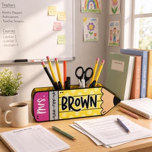 May include: A yellow pencil-shaped desk organizer with the name "BROWN" in bold black letters. The organizer holds pencils, pens, and scissors. A coffee mug, grade book, and other school supplies are on the desk.