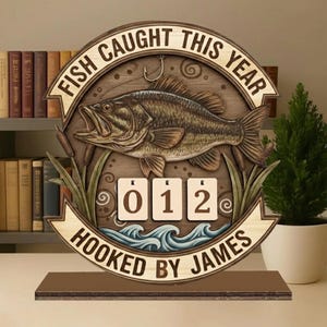 Puede incluir: Letrero de madera con temática de pesca con el texto "FISH CAUGHT THIS YEAR" y "HOOKED BY JAMES". El letrero presenta una talla detallada de un pez, agua y juncos, con fichas numéricas que muestran "012".