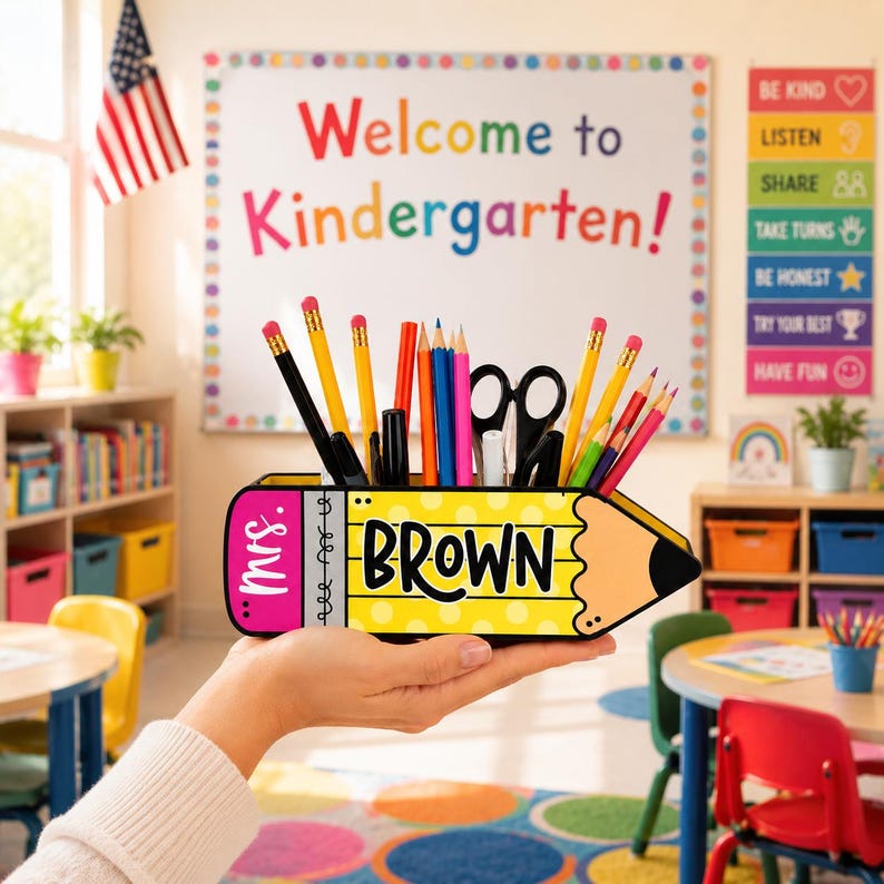 May include: A yellow pencil-shaped desk organizer with the name "BROWN" in black letters. The organizer holds pencils, pens, and scissors. The word "Mrs." is on the pink eraser end. The background is a classroom setting.