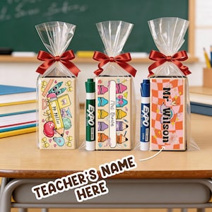 May include: Three gift bags with red bows, each containing a personalized eraser and an Expo dry-erase marker. The erasers are decorated with school-themed illustrations and teacher names. The text "Teacher's Name Here" is also visible.