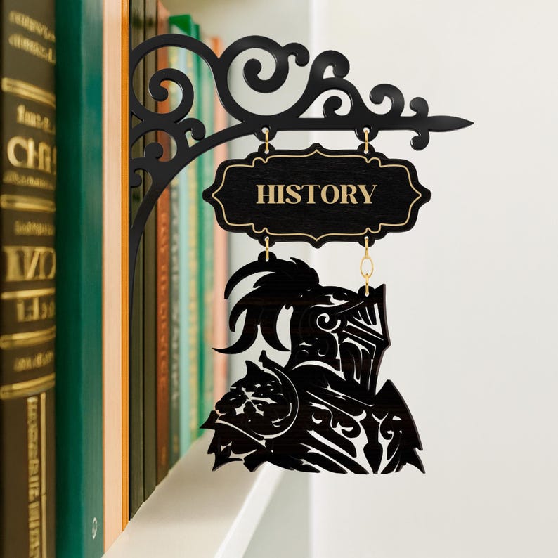 以下が含まれることがあります： 金色の文字で「HISTORY」と書かれた黒い木製の看板が、装飾的なブラケットから吊り下げられています。看板の下には、騎士のヘルメットと鎧のシルエットがあります。看板は本棚の前に表示されています。