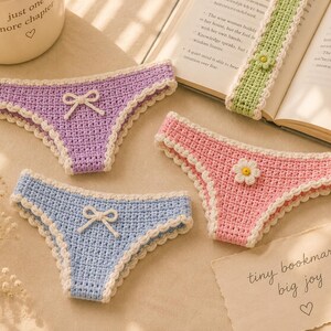 May include: Crocheted bookmarks shaped like underwear in pastel colors: purple, pink, and blue. Each has a white scalloped trim and a bow or flower detail. A green bookmark with a flower is also present. The text "tiny bookmark big joy" is visible.