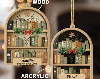 Könnte beinhalten: Zwei dekorative Bücherregal-Ornamente. Eines ist aus Holz, das andere aus Acryl. Jedes hat ein Miniatur-Bücherregal mit farbigen Buchrücken, floralen Akzenten und einer roten Schleife. Das Holzornament trägt die Aufschrift "Amellia Boston Book Club". Das Acrylornament trägt die Aufschrift "Daniel New York Book Club".