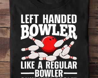 May include: Black t-shirt with a bowling theme. The shirt features the text "LEFT HANDED BOWLER" above a red bowling ball and white bowling pins. Below the ball and pins, the text reads "LIKE A REGULAR BOWLER - ONLY WAY COOLER."