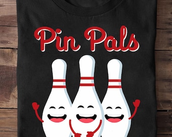 May include: Black t-shirt featuring the text "Pin Pals" in red script with a white outline. Below the text are three smiling bowling pins with red accents and arms.