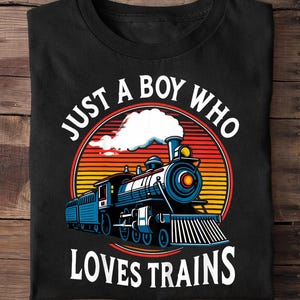 Könnte beinhalten: Schwarzes T-Shirt mit einem Zug-Motiv und dem Text "JUST A BOY WHO LOVES TRAINS". Der Zug ist blau mit einem roten und gelben Sonnenuntergangshintergrund. Der Text ist weiß.