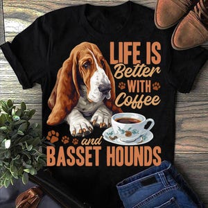 May include: Black t-shirt with a Basset Hound graphic and the words "LIFE IS Better WITH Coffee and BASSET HOUNDS." The design includes a coffee cup and paw prints. The dog is depicted in brown, white, and black.