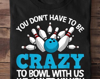 May include: Black t-shirt with a bowling theme. The shirt features a blue bowling ball and white bowling pins. Text on the shirt reads "YOU DON'T HAVE TO BE CRAZY TO BOWL WITH US WE CAN TRAIN YOU."