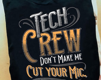 Puede incluir: Camiseta negra con las palabras "TECH CREW" en letras blancas y naranjas. El texto "DON'T MAKE ME CUT YOUR MIC" está debajo. La camiseta está doblada sobre una superficie de color claro.
