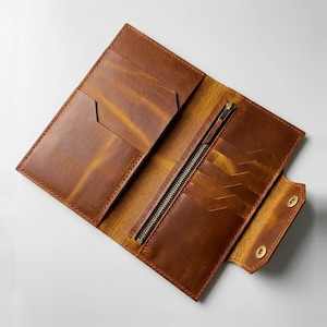 May include: Open, brown leather wallet with multiple card slots, a zippered compartment, and snap closure. The wallet has a distressed finish and visible stitching. The interior is a lighter shade of brown than the exterior.