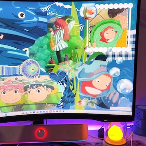 May include: A computer monitor displaying colorful anime-style artwork with characters and aquatic themes. A keyboard, mouse, and speaker are in the foreground. A small, yellow, lemon-shaped lamp sits to the right of the monitor. The desk has a floral mousepad and a pink cloud-shaped wrist rest.