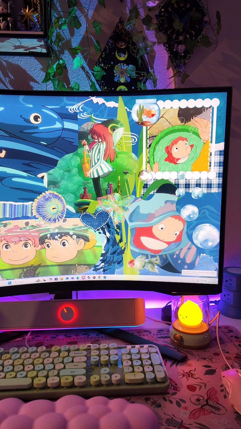 May include: A computer monitor displaying colorful anime-style artwork with characters and aquatic themes. A keyboard, mouse, and speaker are in the foreground. A small, yellow, lemon-shaped lamp sits to the right of the monitor. The desk has a floral mousepad and a pink cloud-shaped wrist rest.
