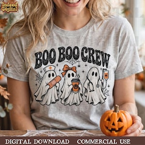 Könnte beinhalten: Ein graumeliertes T-Shirt mit dem schwarzen Schriftzug BOO BOO CREW. Die Grafik zeigt drei weiße Geister: einer trägt eine Krankenschwesterhaube und hält ein Pflaster, einer hat eine orangefarbene Schleife und einen Kürbis-Kaffeebecher, einer ein Stethoskop.