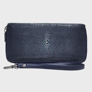 Könnte beinhalten: Eine rechteckige marineblaue Clutch mit einer texturierten Rochenhaut-Optik und einem markanten zentralen Muster aus größeren, helleren Perlen. Die Geldbörse verfügt über eine passende marineblaue Handschlaufe aus Leder mit einem silbernen Metallverschluss.