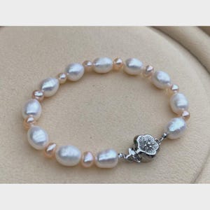 Può includere: Un delicato braccialetto con una serie di perle d'acqua dolce bianche e rosa. Le perle sono infilate, alternando dimensioni e colore, e fissate con una chiusura floreale argentata. Un gioiello classico.